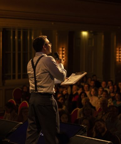 Simon Hauser moderiert vor Publikum in einem Veranstaltungssaal